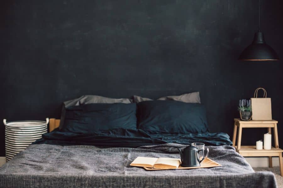 Cozy bedroom with black accent wall, dark bedding, and bedside table setup.