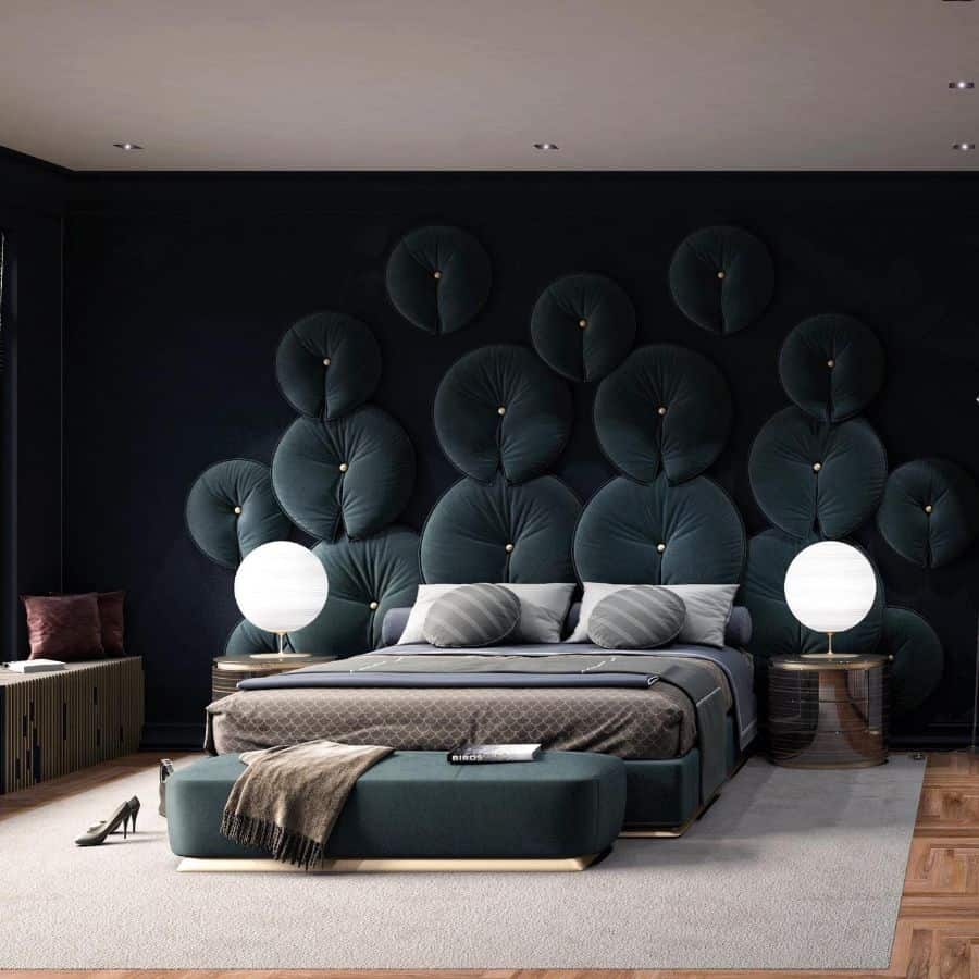 Luxurious bedroom with black cushioned wall, modern bed, and round bedside lamps.