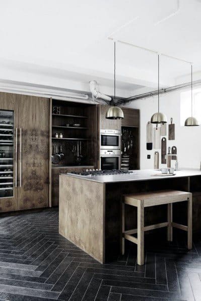 Modern kitchen with dark herringbone tile flooring, wooden cabinetry, and sleek stainless steel appliances