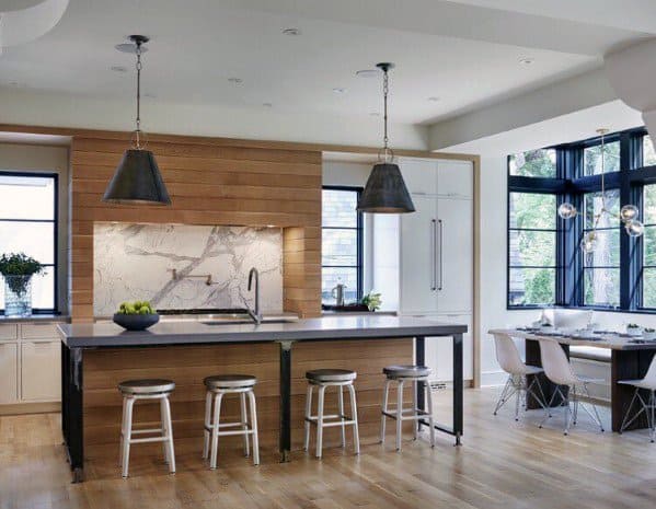 Modern kitchen with large black pendant lights above an island, wood accents, and stylish dining area with large windows