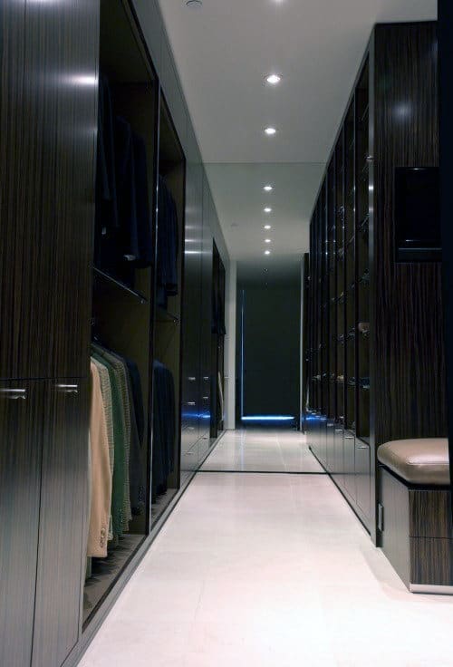 A modern walk-in closet with dark wood shelves, hanging clothes, and a cushioned bench