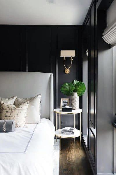 Elegant black bedroom with paneled walls, neutral bedding, and a gold-accented side table.