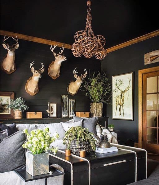 A rustic living room with black-painted walls, deer antler decorations, a unique chandelier, and elegant plants, creating a cozy, nature-inspired atmosphere