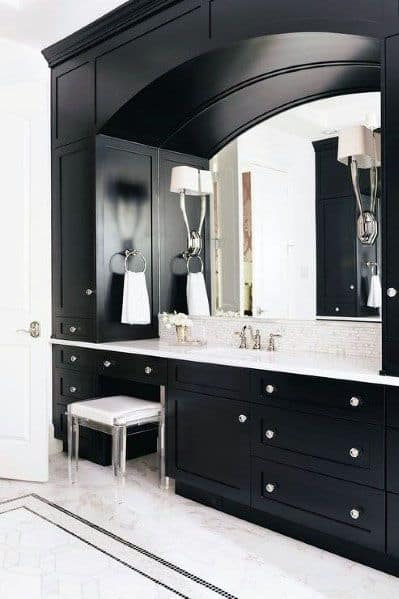 Bathroom with black vanity, arched mirror, and white marble backsplash.