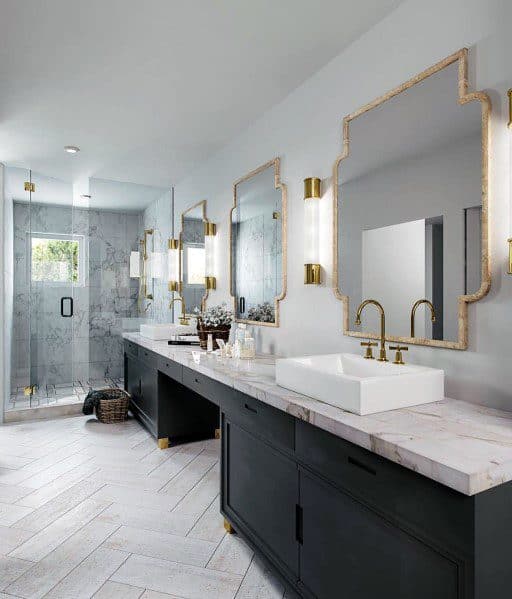 Double vanity bathroom with gold-trimmed mirrors, marble countertop, and glass shower enclosure.