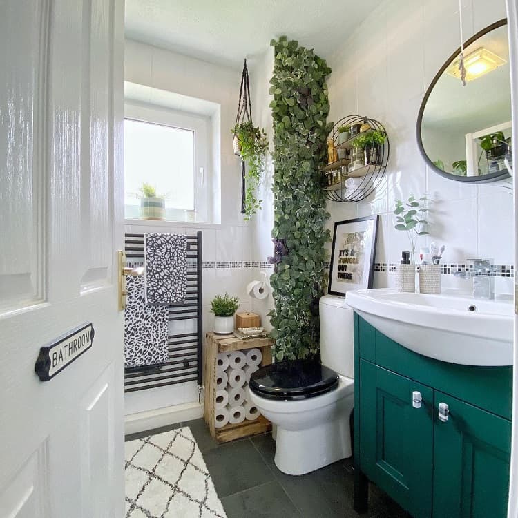 Modern bathroom with floor-to-ceiling artificial plant, green vanity, and decorative shelves.