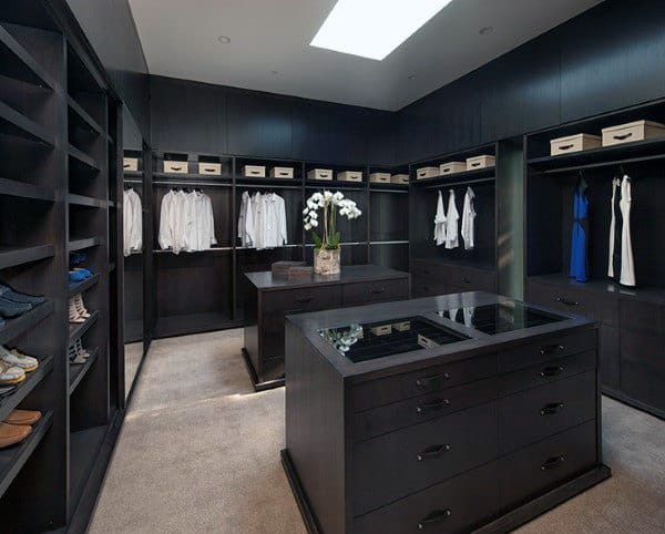 Spacious walk-in closet with dark wood shelves, neatly arranged clothing, and a central island with orchids