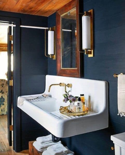 Bathroom with blue walls, white vintage sink, and brass lighting fixtures.