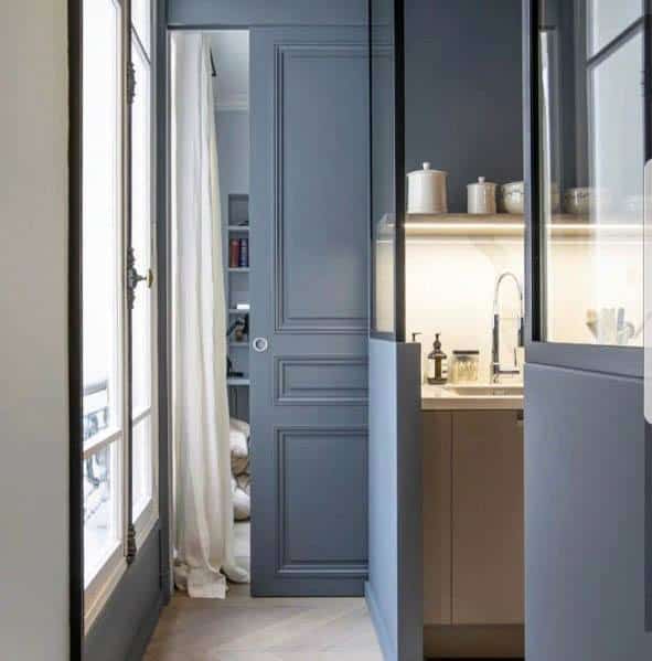 Elegant blue pocket door in a modern kitchen, leading to a pantry with soft lighting, shelves, and neutral decor