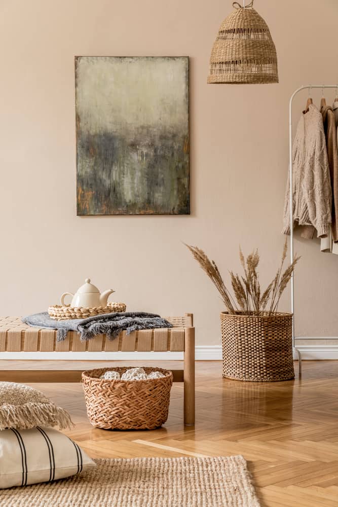 Cozy room with brown woven decor, beige tones, a bench, teapot, abstract painting, and clothes rack