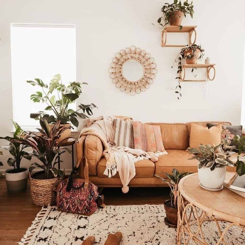 Cozy living room with a brown tan sofa, green plants, a round mirror, and a woven rug and table