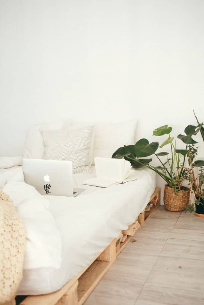 Minimalist boho bedroom with pallet bed, cozy whites, and lush greenery.