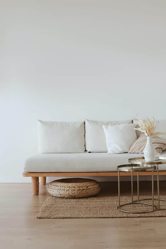 Boho minimalist living room with a light wood sofa, neutral cushions, woven rug, and gold nesting tables for decor