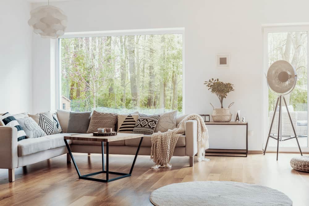 Bright boho living room with a cozy sectional sofa, textured cushions, wooden coffee table, and large windows with greenery views