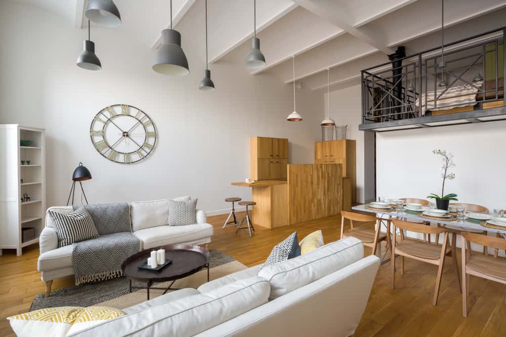 Open-concept living room with white sofas, wooden dining set, industrial loft design, and modern lighting fixtures