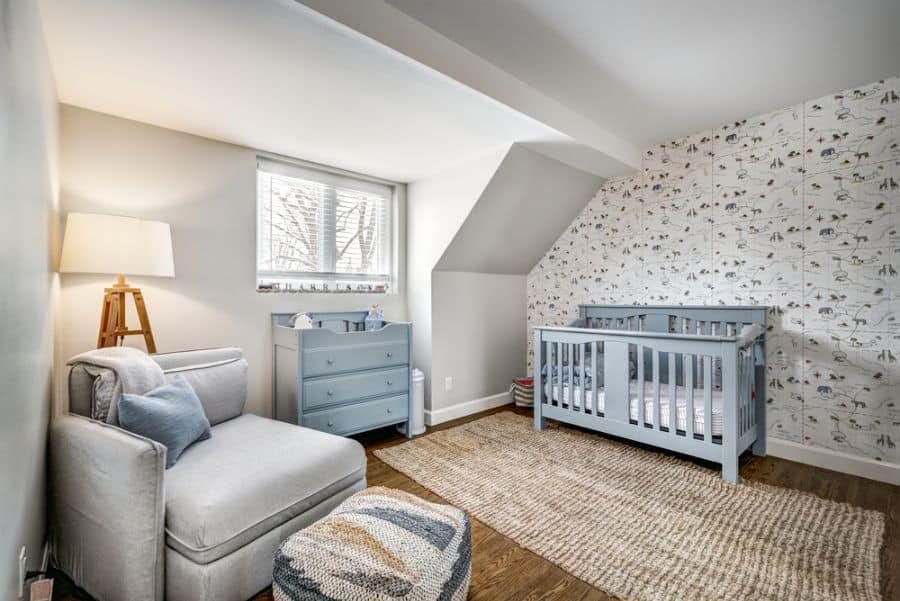 Cozy baby boy's attic room with blue crib, armchair, and animal-themed wallpaper.