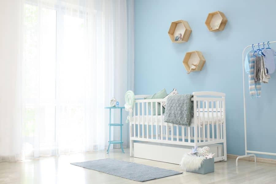 Contemporary baby boy's room with light blue walls, white crib, and geometric wall shelves.