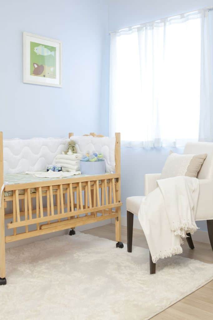 Simple baby boy's room with light blue walls, wooden crib, and cozy chair.