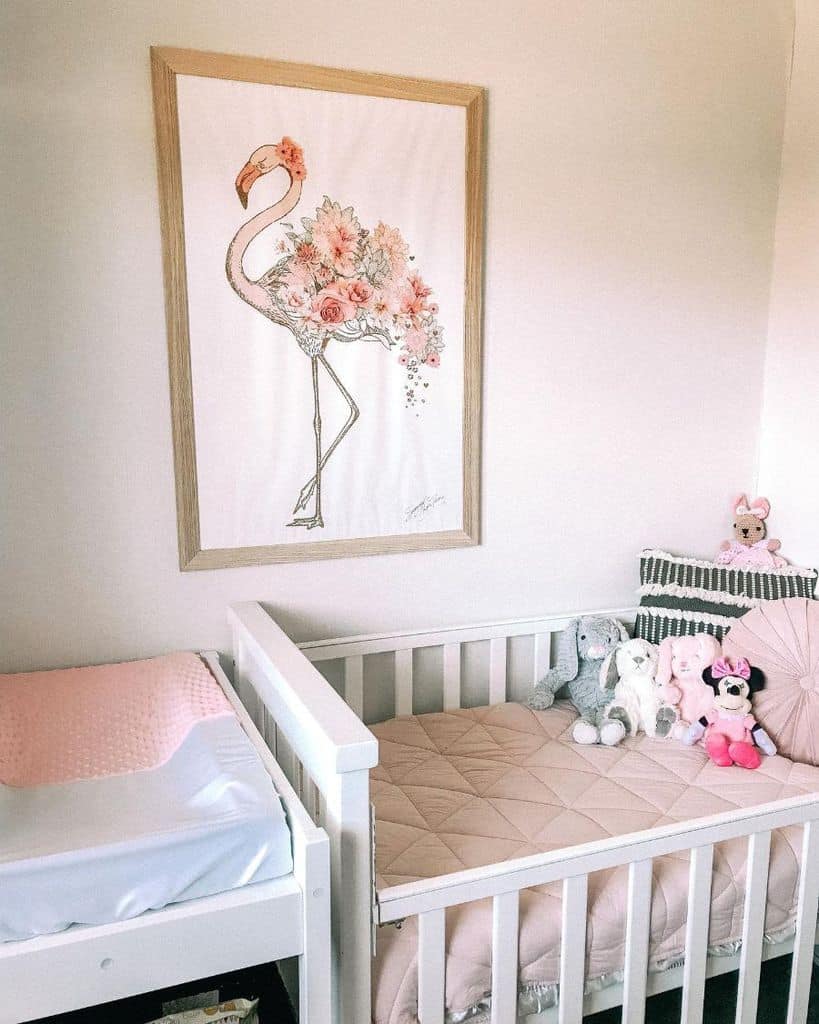 Delicate baby girl's room with floral flamingo wall art, soft pink bedding, and plush toys.