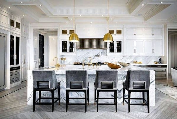 Luxurious kitchen with brass pendant lights above a marble island, gray bar stools, and elegant design elements