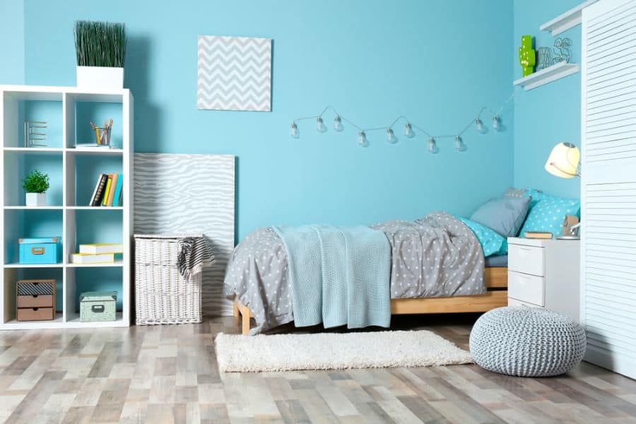 Light blue kids' bedroom with cozy bedding, shelving, and decorative string lights.