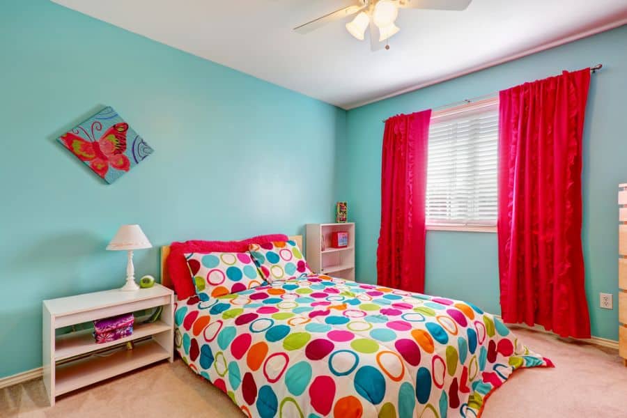 Bright kids' bedroom with light blue walls, colorful polka dot bedding, and red curtains.