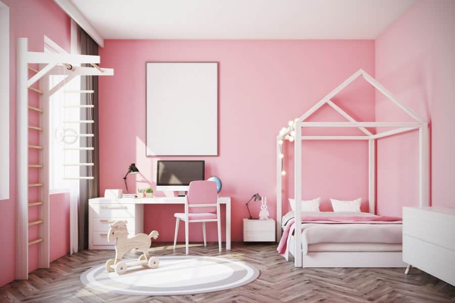 Pink kids' bedroom with a four-poster bed, white desk, and wooden floor.