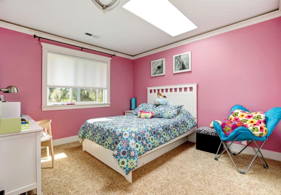 Vibrant pink bedroom with floral bedding, blue accent chair, and cozy carpet flooring.