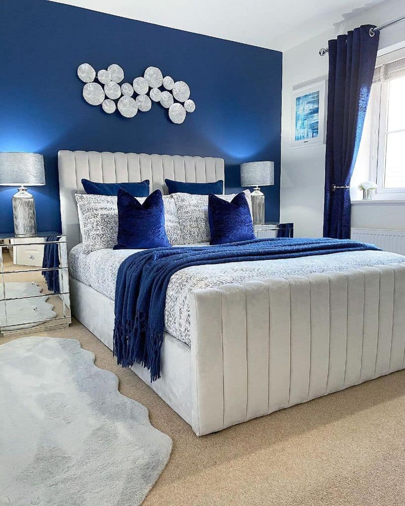 Luxurious blue bedroom with tufted bed, mirrored bedside tables, and plush decor.