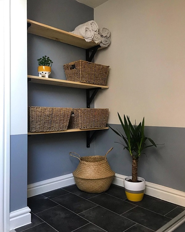 Wooden bathroom shelves with wicker baskets and rolled towels, potted plant on tiled floor.