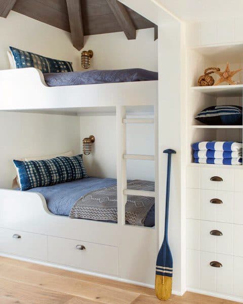 White bunk bed with built-in storage, nautical decor, and cozy bedding.