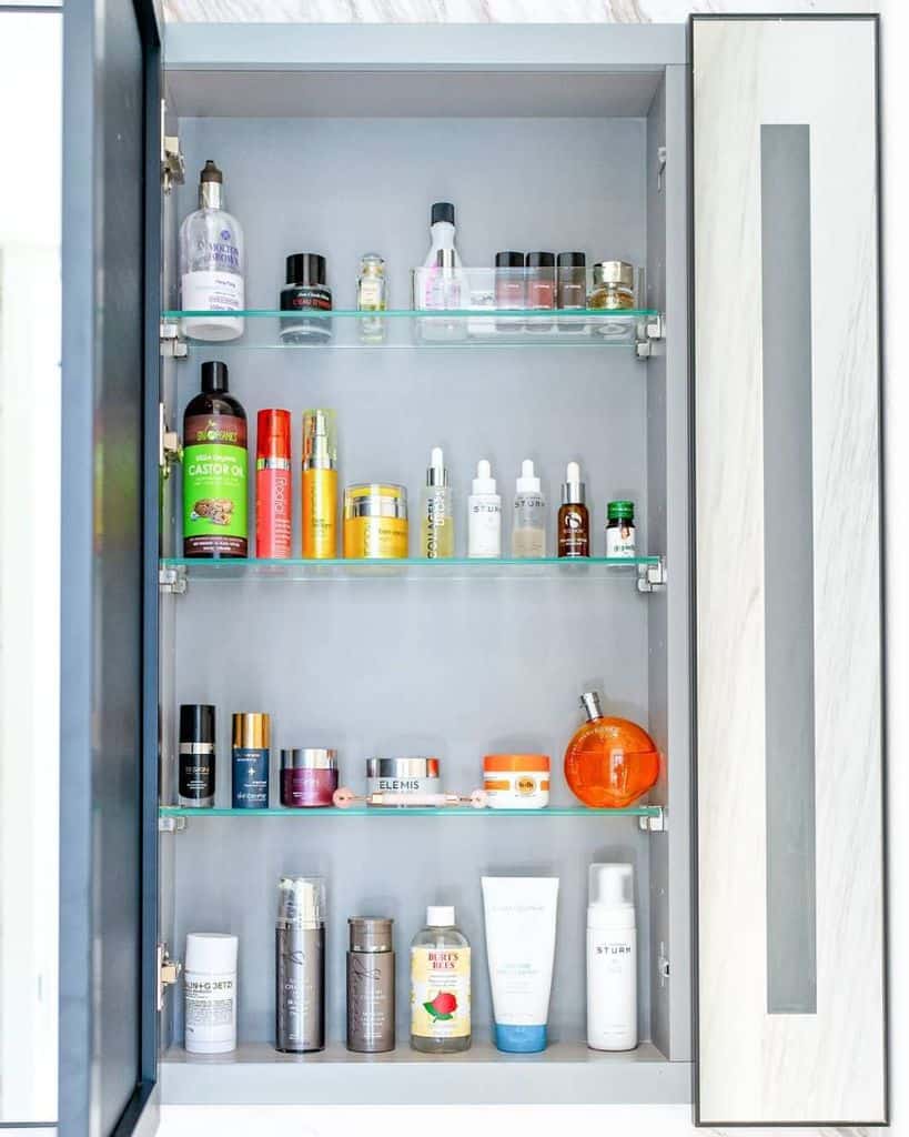 Bathroom cabinet with organized skincare, haircare, and body products on glass shelves.