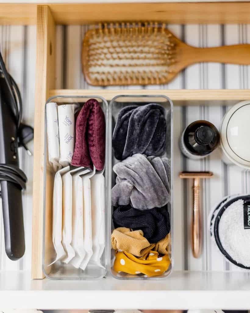 Organized bathroom drawer with hair accessories, tampons, a wooden brush, and grooming tools.