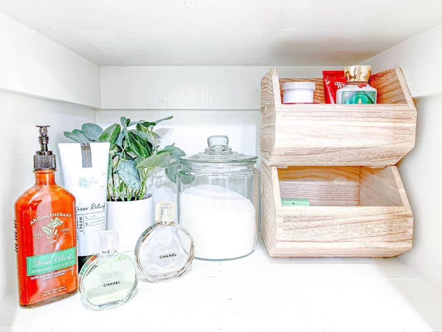 Bathroom shelf with wooden bins, glass jar, perfumes, and lotions for organized storage.