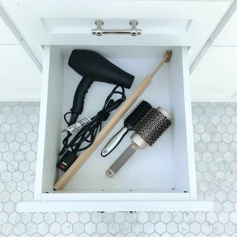 Bathroom cabinet drawer with a hair dryer, brush, and grooming tools neatly organized.