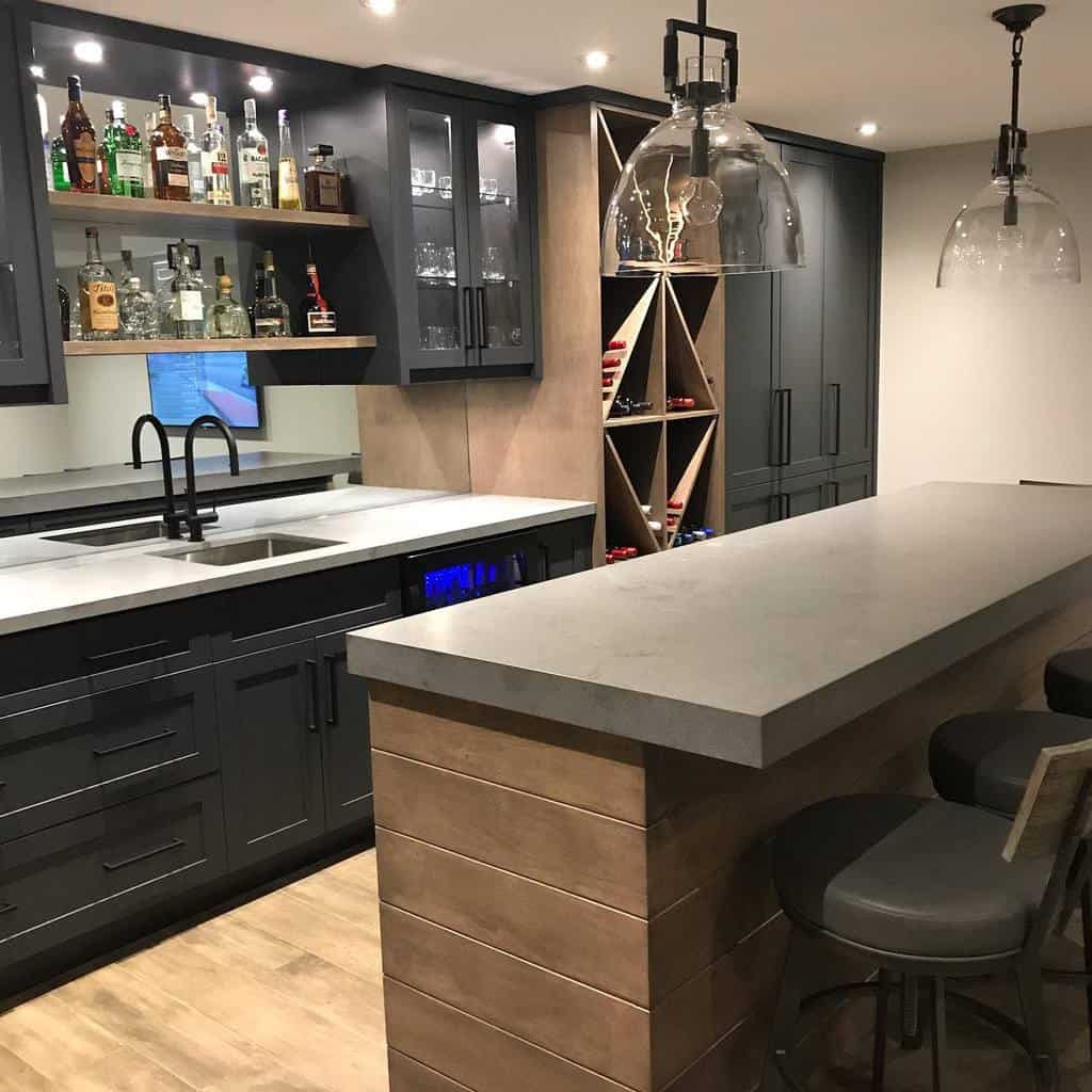 Modern wet bar with black cabinets, concrete countertop, wine storage, and glass pendant lights.