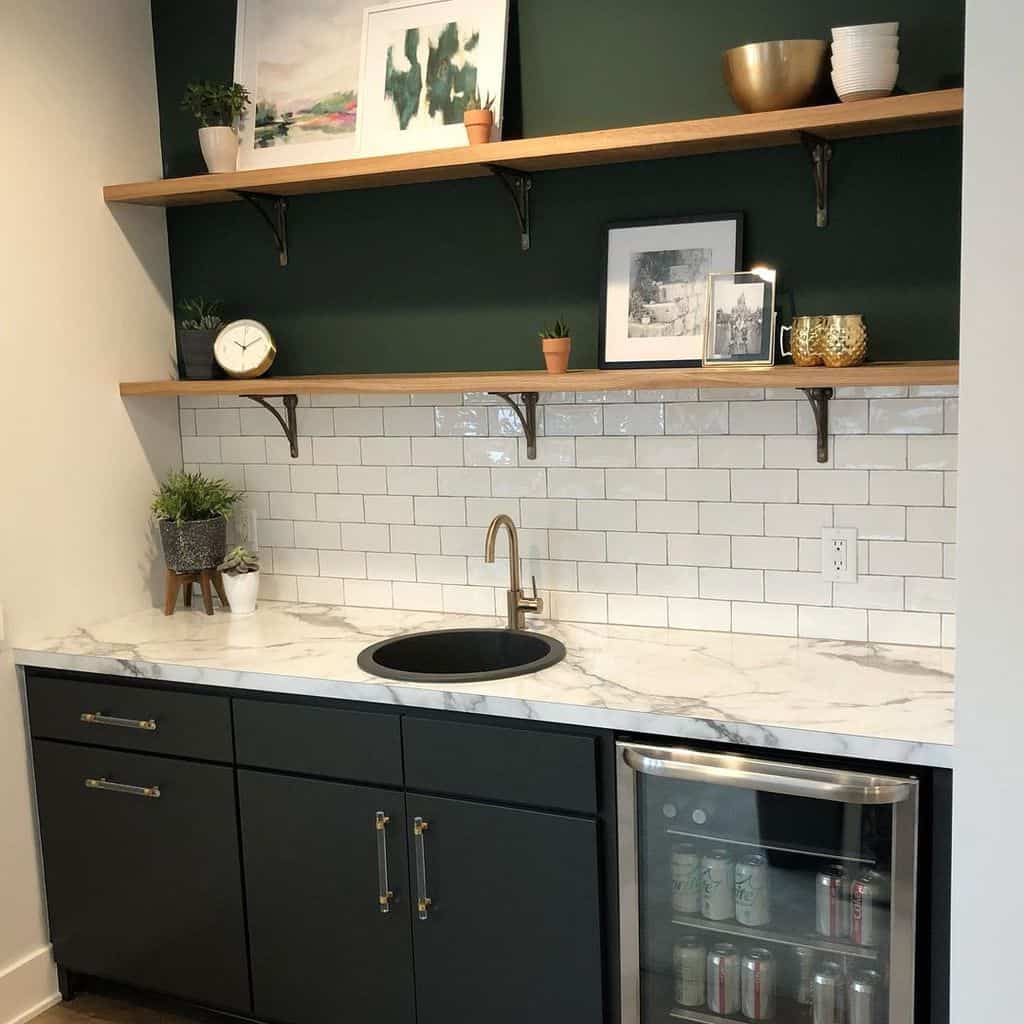 Compact wet bar with green cabinets, marble countertop, open shelves, and subway tile backsplash.