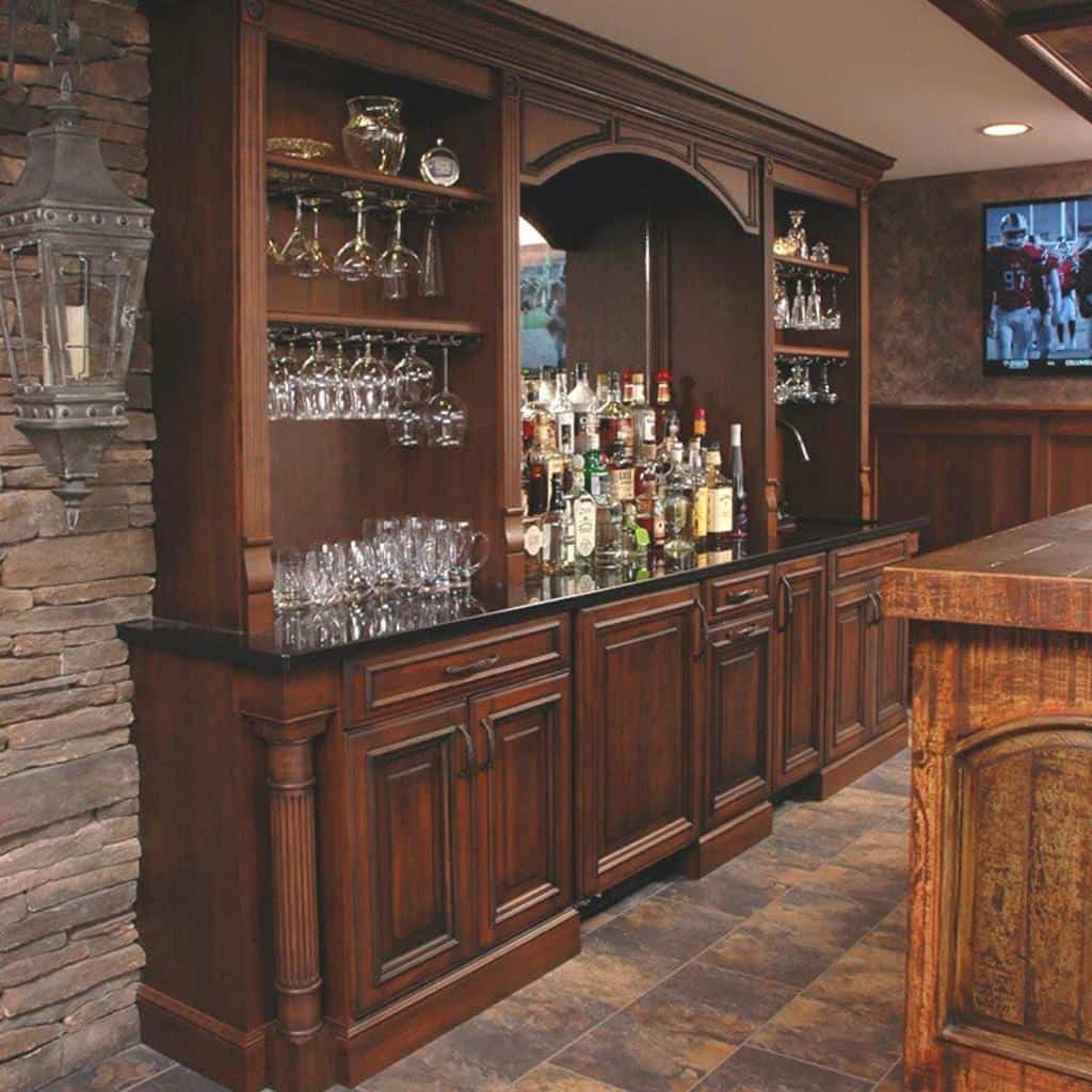 Traditional wet bar with dark wood cabinetry, glassware display, and stone accent wall.