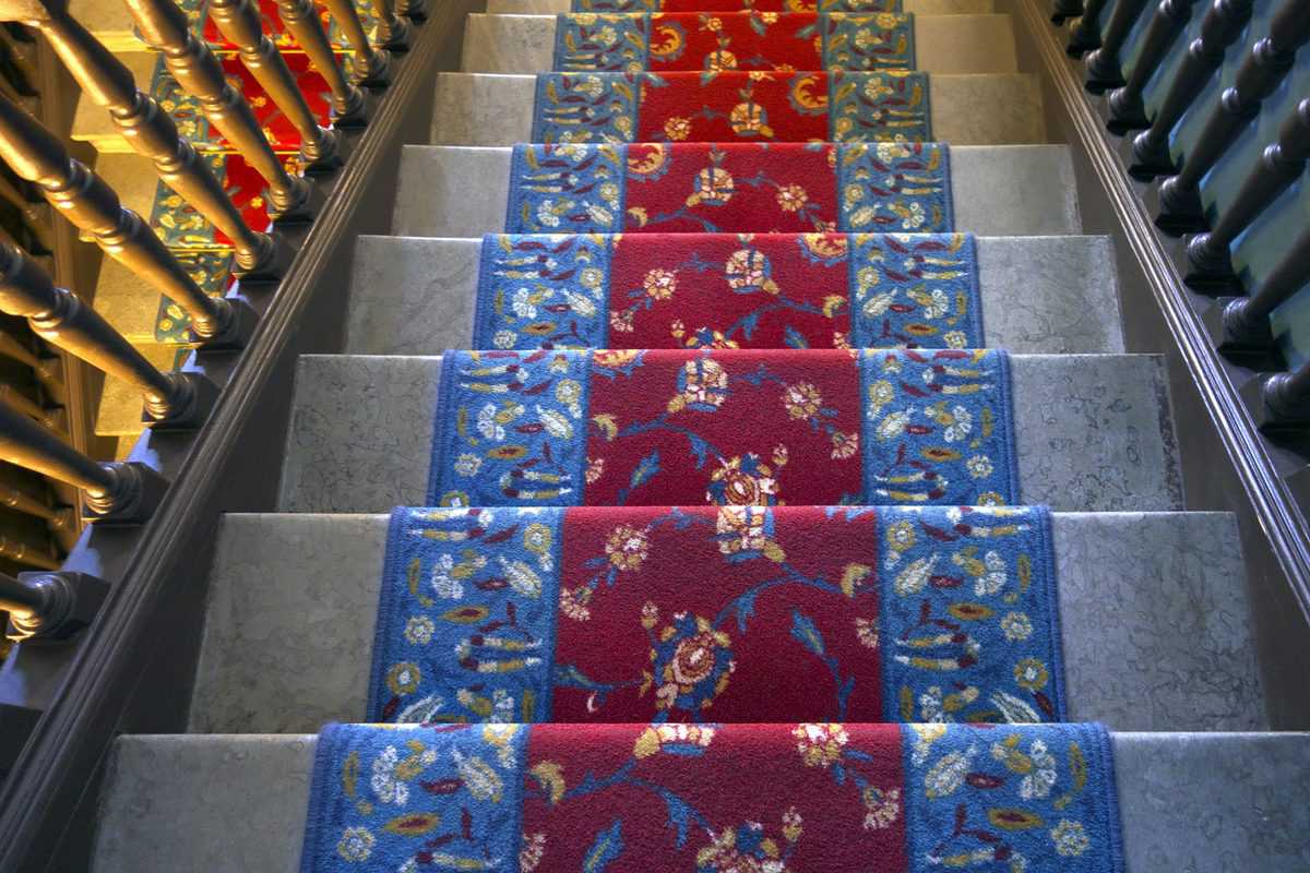 Marble staircase with vibrant red and blue floral-patterned carpet runner.