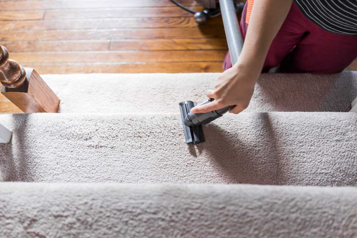 Person vacuuming beige carpeted stairs with a handheld vacuum cleaner.