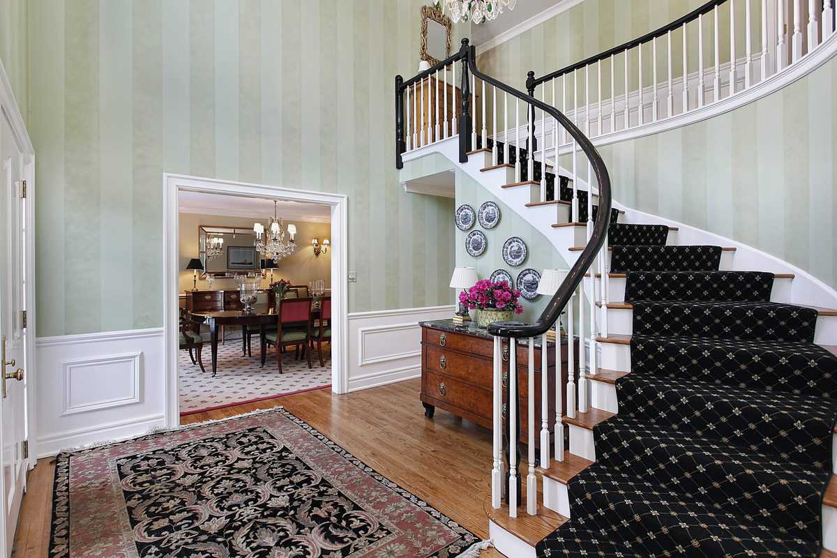 Elegant foyer with a black patterned carpeted staircase and a view of the dining room.