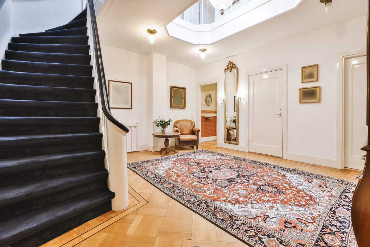 Bright foyer with dark carpeted staircase, ornate rug, and elegant decor accents.