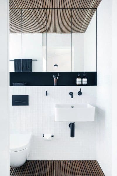 Minimalist bathroom with white walls, wood accents, a small sink, and mirrors above