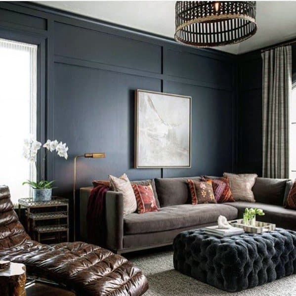 Elegant living room with dark walls, velvet sofa, tufted ottoman, and leather lounge chair.