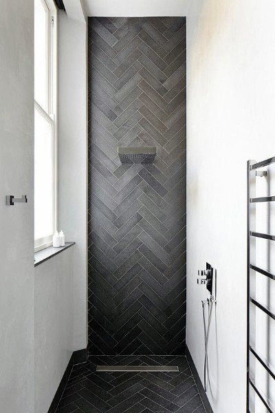 Black herringbone patterned tile shower with built-in shelf and minimalist chrome fixtures.