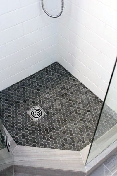 Hexagonal dark grey tile shower floor with glass enclosure and white subway tile walls.