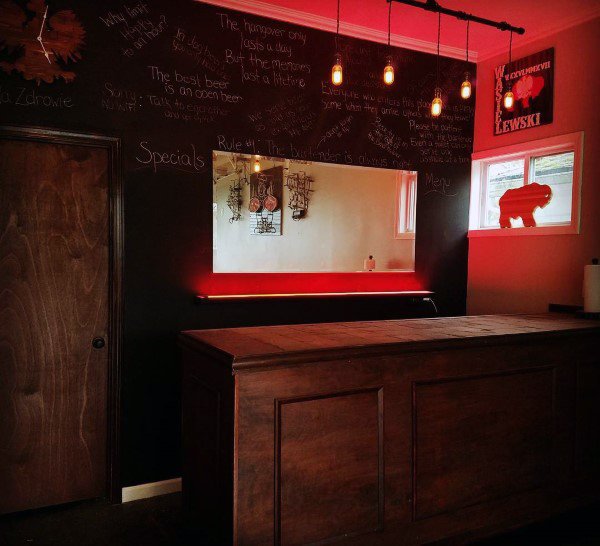 Garage bar with chalkboard walls, wooden counter, red accent lighting, and hanging pendant lights.