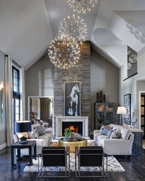 Modern living room with high ceiling, large chandelier, fireplace, and elegant décor; neutral tones and cozy seating