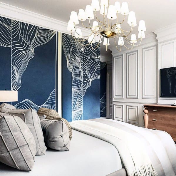 Sophisticated bedroom with blue patterned wallpaper, gray bedding, and a gold chandelier.