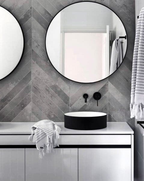 Modern bathroom with circular mirrors, grey chevron tiles, and white vanity